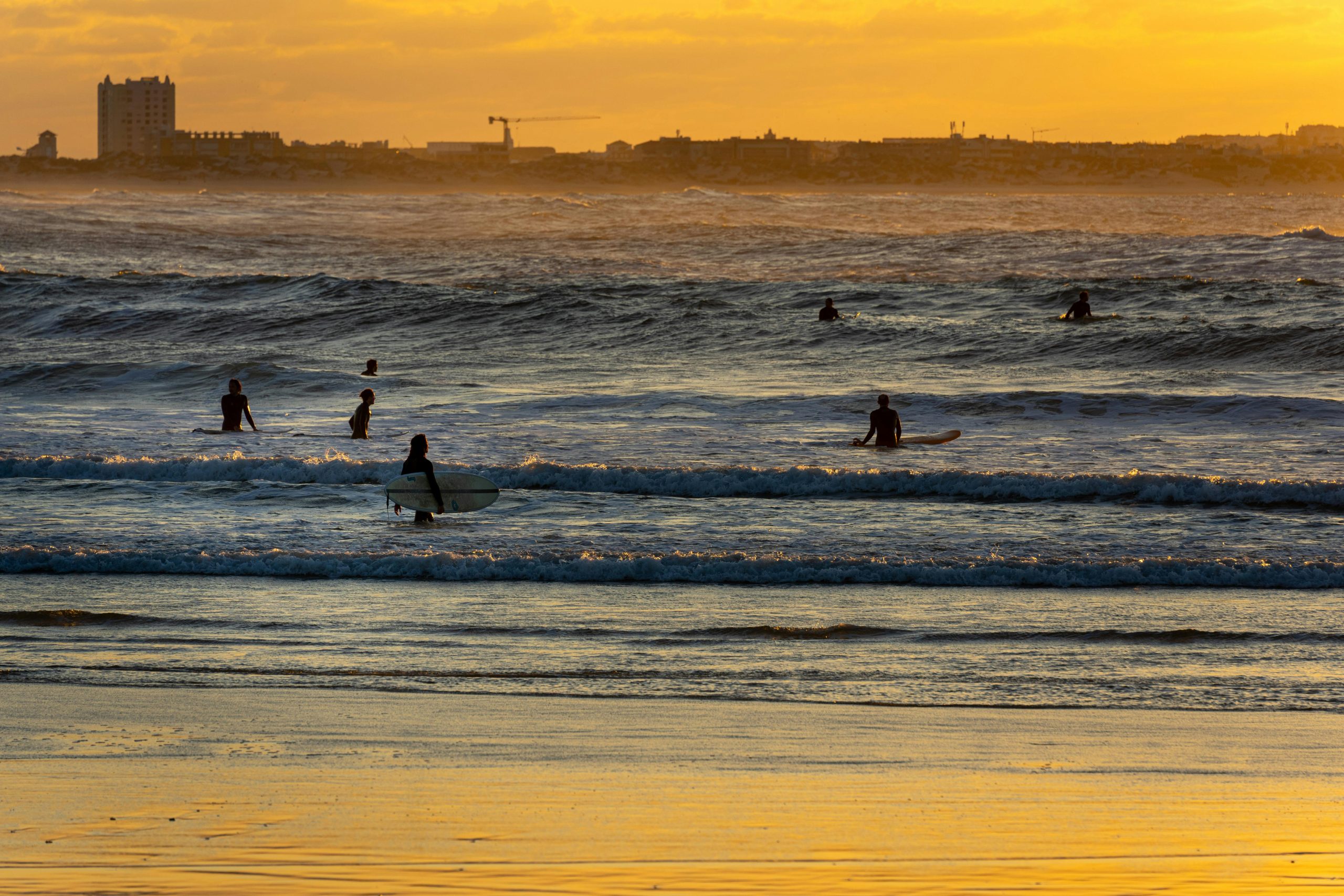 Silhouetted surfers catching waves at sunset on a vibrant, golden beach.