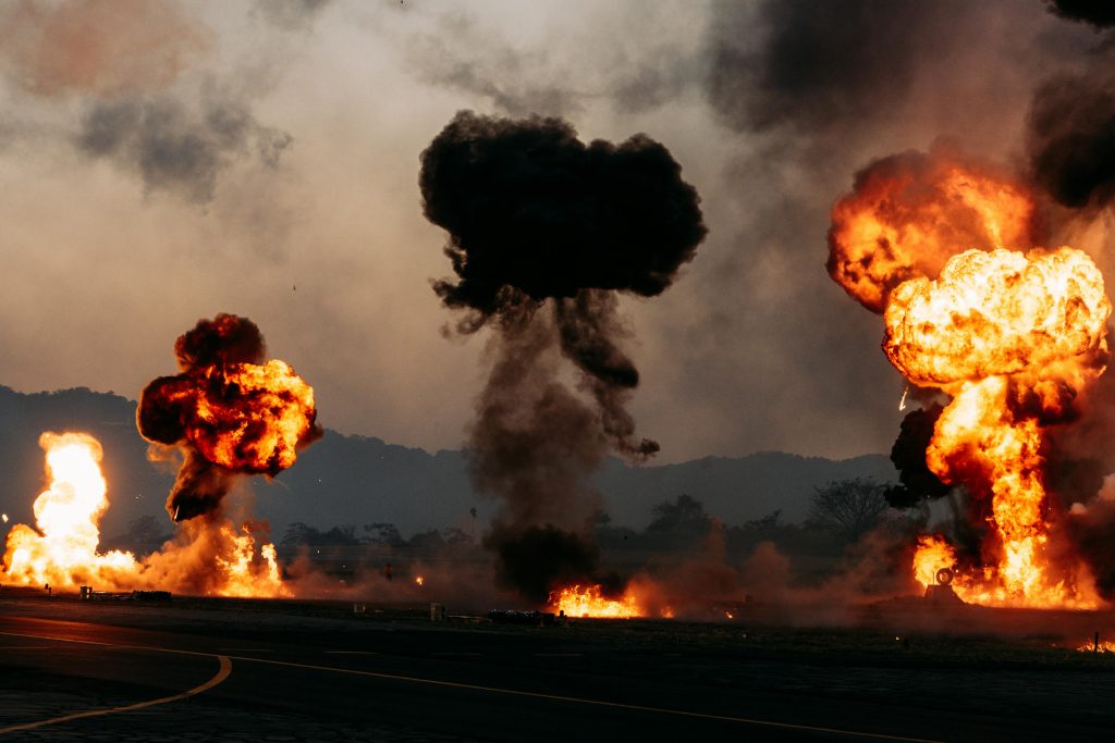 Intense outdoor scene with multiple fiery explosions creating dramatic clouds.
