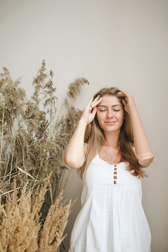 A serene woman with a prosthetic arm stands by dried plants, embodying beauty and resilience.