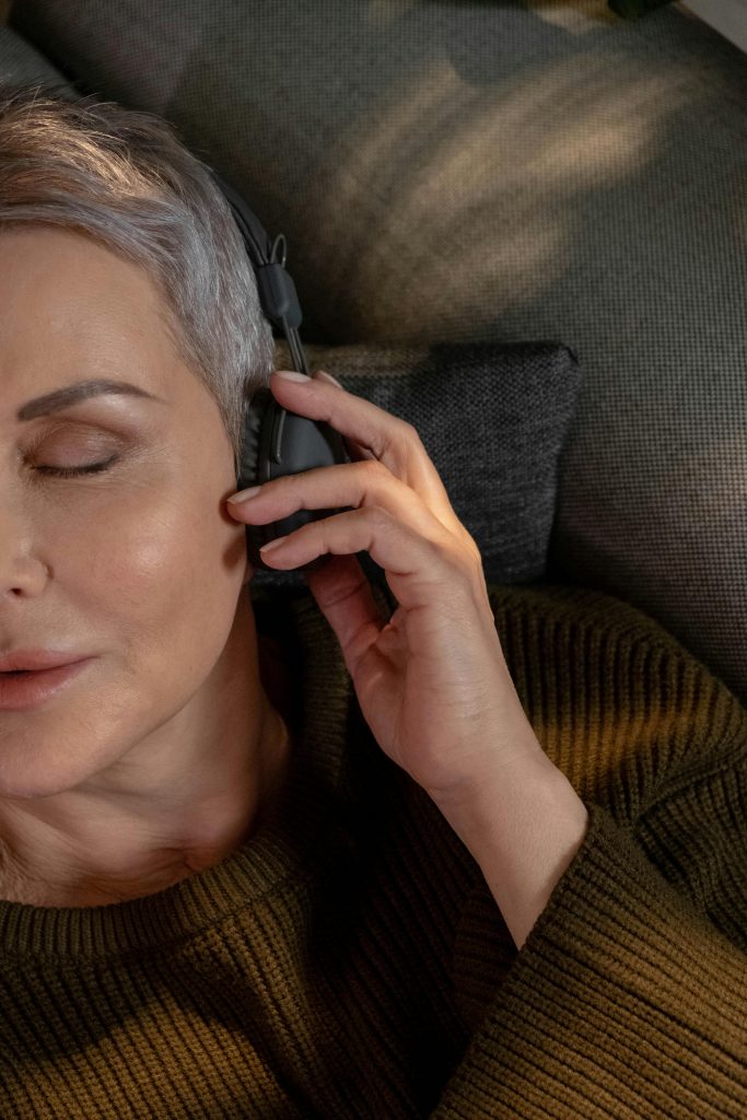 A serene scene of a mature woman with gray hair listening to music on headphones, lying on a sofa.