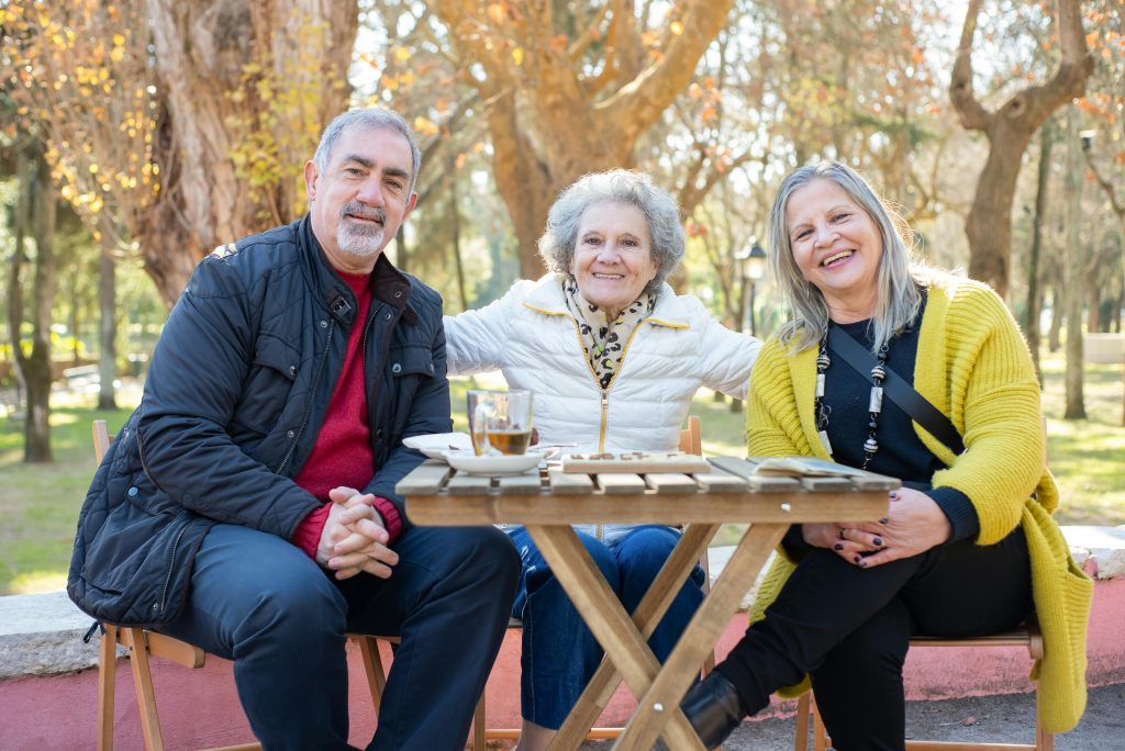 Three smiling seniors together enjoying a sunny day in a park in Portugal.