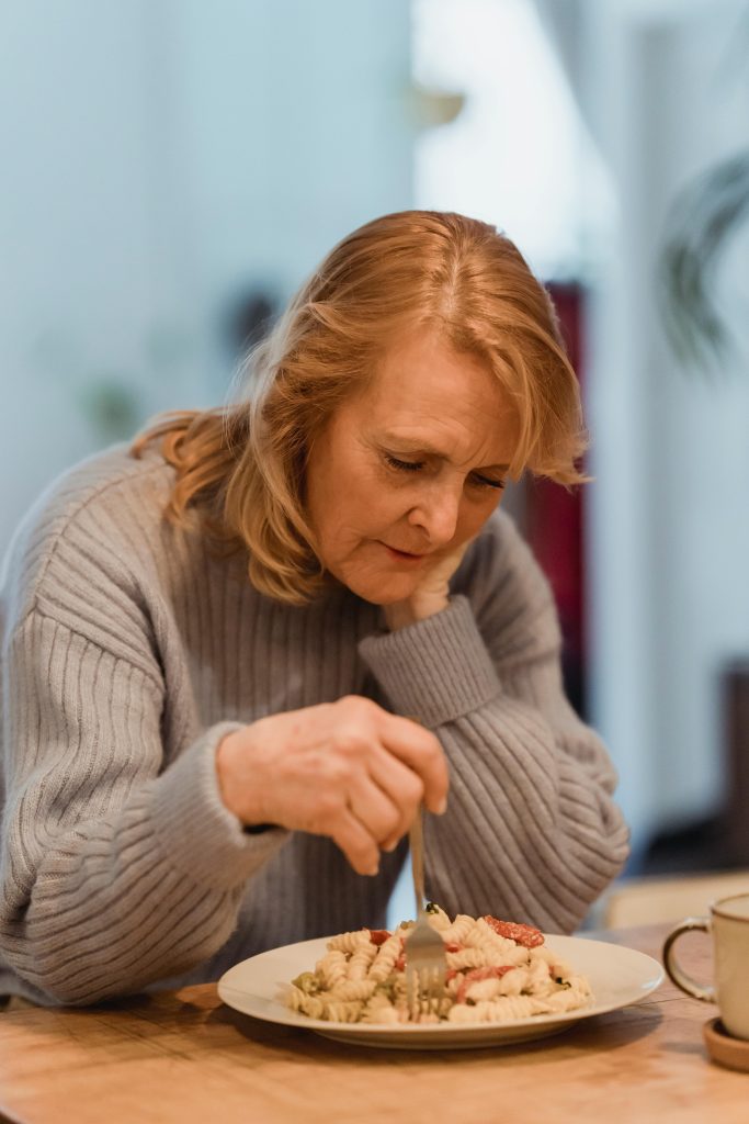 Senior woman in a cozy setting eating pasta, reflecting comfort and solitude.